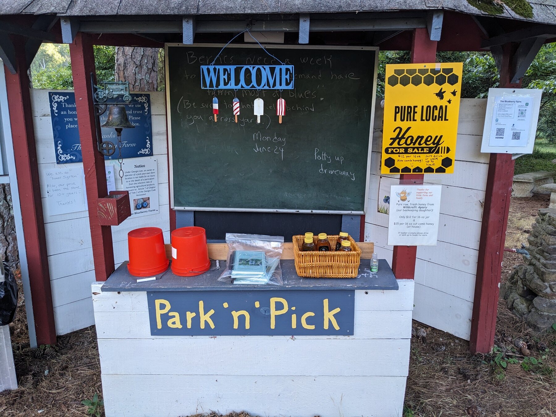 The Park 'n' Pick kiosk in 2024 with chalkboard, buckets, printed notices, and newer payment information
