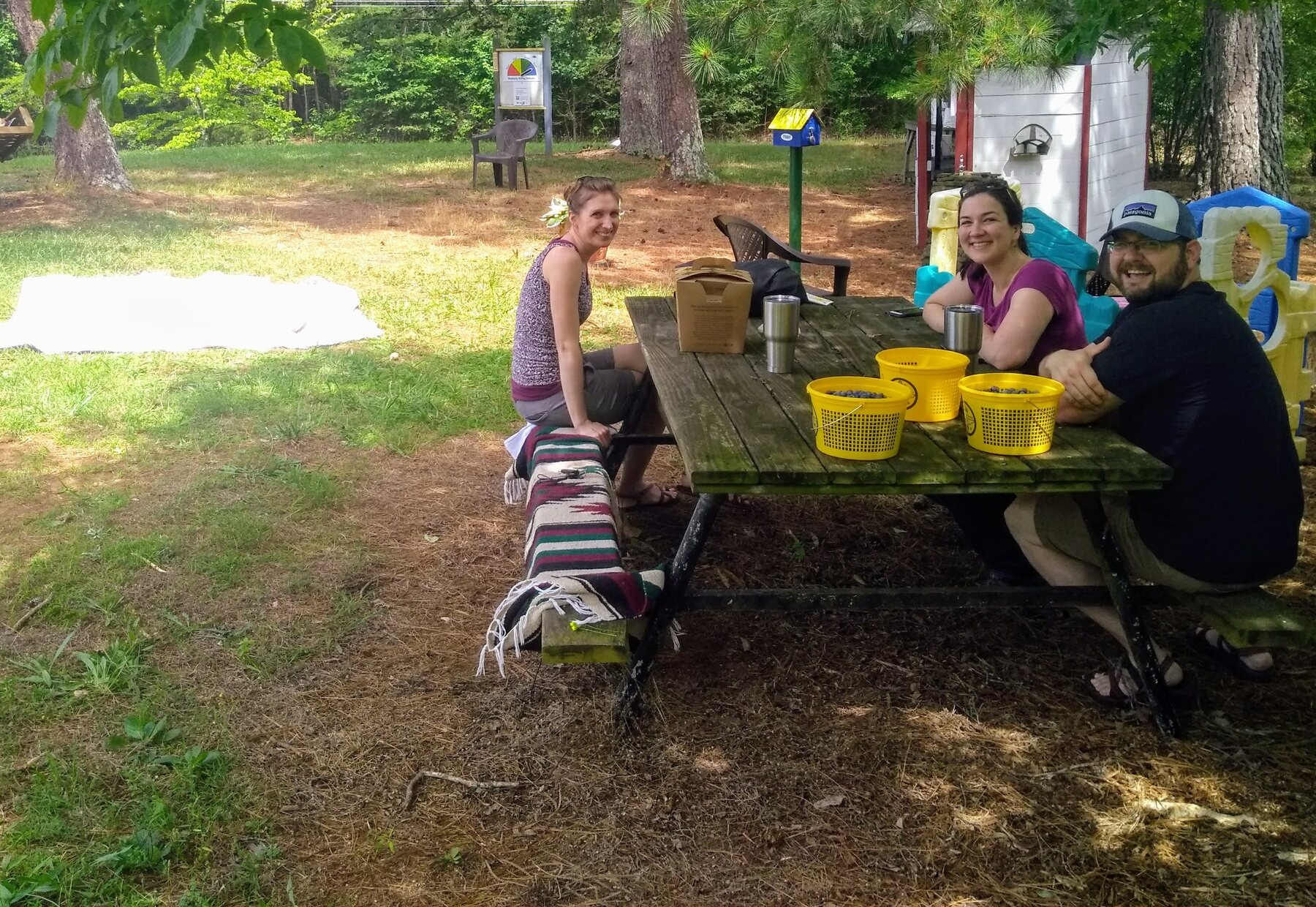 Visitors relaxing at a shaded picnic table with picking baskets